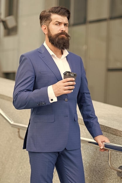 Jefe serio con vello facial sin afeitar en traje de moda formal beber café de la mañana al aire libre cafeína