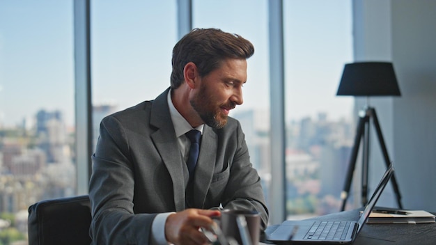 El jefe sonriente hablando con la computadora portátil conectándose en línea el gerente tranquilo bebiendo café