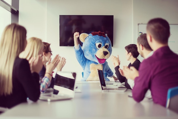 Jefe vestido como oso de peluche divirtiéndose con gente de negocios en la oficina corporativa moderna