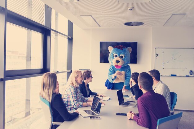 Jefe vestido como oso de peluche divirtiéndose con gente de negocios en la oficina corporativa moderna