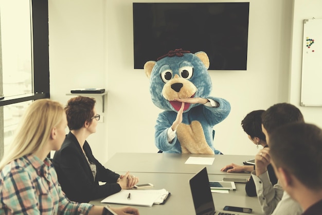 Jefe vestido como oso de peluche divirtiéndose con gente de negocios en la oficina corporativa moderna