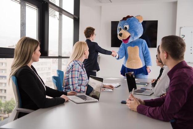 Jefe vestido como oso de peluche divirtiéndose con gente de negocios en la oficina corporativa moderna