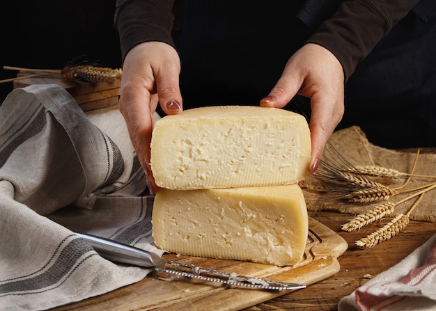 Jemandes Hände legen ein Stück frischen hausgemachten Käse auf ein Holzbrett aus der Nähe