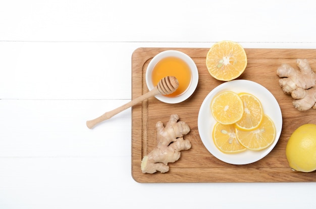 Jengibre con limonada y té de hierbas en un escritorio de madera sobre fondo blanco.