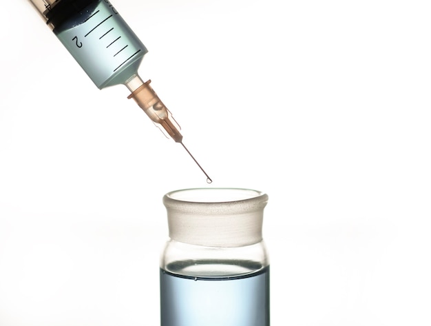 Una jeringa y un frasco de vidrio con un líquido azul, una foto sobre el tema de la medicina y la investigación científica.