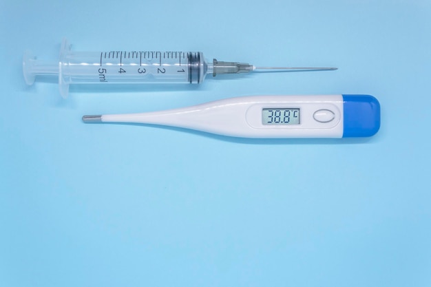 Jeringa de inyección y termómetro digital que muestra alta temperatura sobre el concepto de prevención de covid de fondo azul