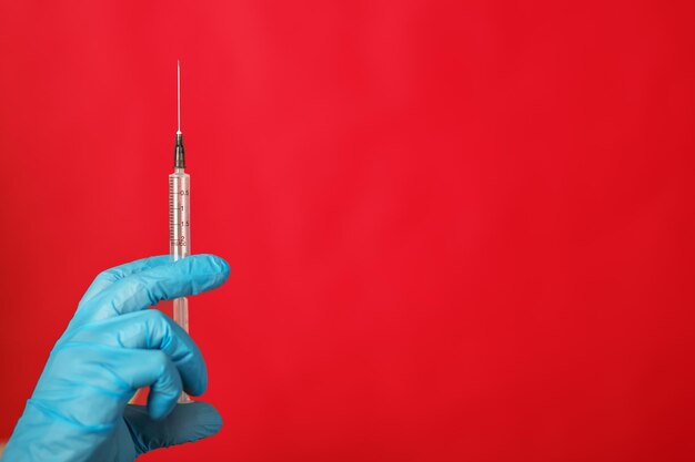 Foto jeringa médica para inyección en la mano de un médico con un guante sobre un fondo rojo