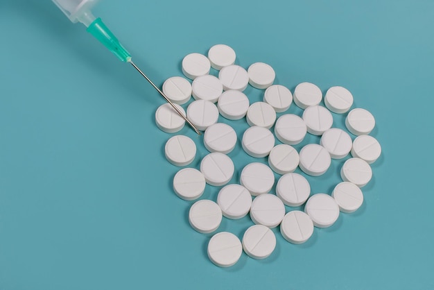 Jeringa y pastillas con forma de corazón sobre fondo azul.