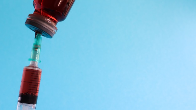 Foto una jeringa sobresale de una botella de líquido rojo. aislado en un fondo azul.