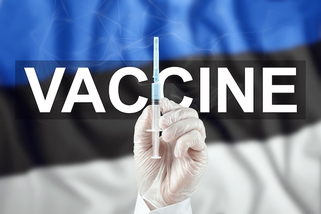 Una jeringa con una vacuna en la mano del médico en el contexto de la bandera de Estonia. Virus corona COVID-19, protección inmunológica, tratamiento contra la infección por nCoV 2019, vacunación.