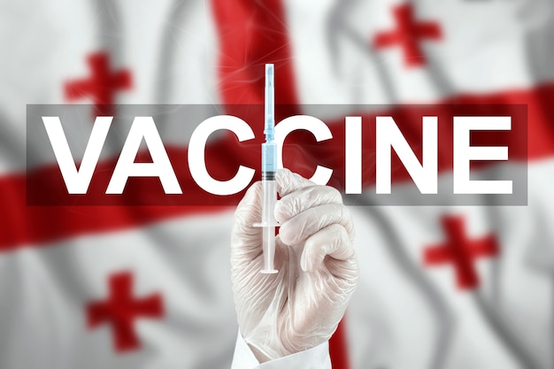 Una jeringa con una vacuna en la mano del médico en el contexto de la bandera de Georgia. Virus corona COVID-19, protección inmunológica, tratamiento contra la infección por nCoV 2019, vacunación.