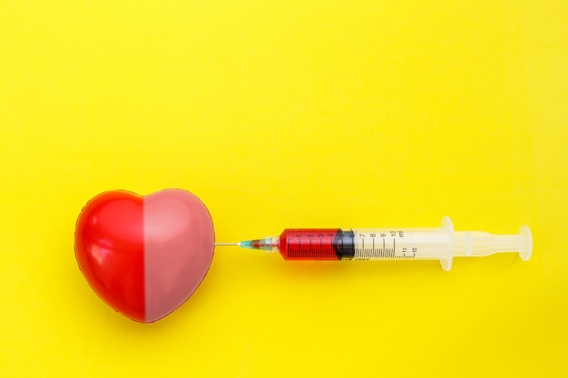 Foto jeringa de vista superior da medicina a forma de corazón rojo sobre fondo amarillo