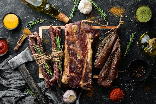 Jerky getrocknetes Kalbfleisch gesalzenes Schweinefleisch und Rosmarin-Räucherwürste Snacks für Bier Auf einem schwarzen Steinhintergrund Ansicht von oben