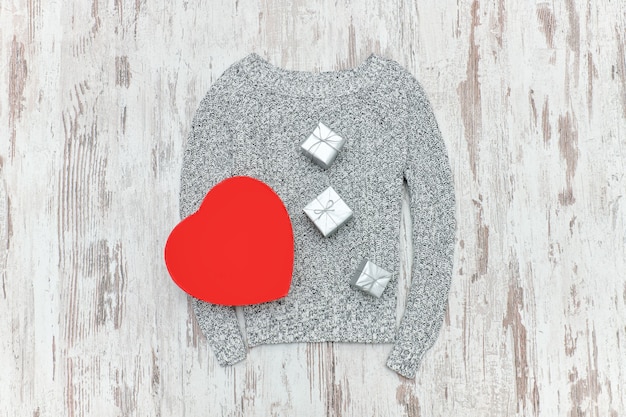 Jersey de punto gris, en forma de corazón rojo y cajas de regalo plateadas. Concepto de moda