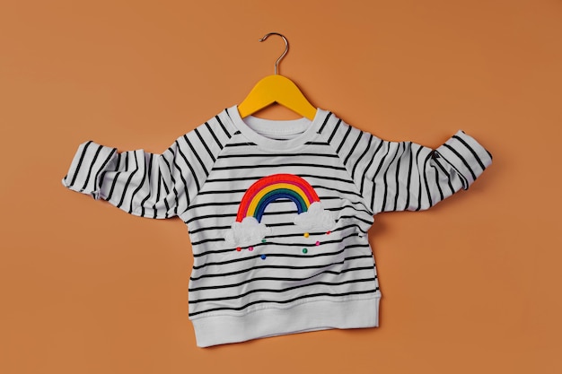 Jersey de rayas con arcoíris en percha sobre fondo naranja. Traje de niños lindos. Ropa infantil para otoño o primavera.