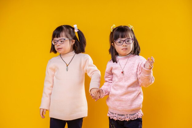 Foto jersey suave y cálido. dos hermanas jóvenes de pie juntos y tomados de la mano y con gafas transparentes para problemas de visión
