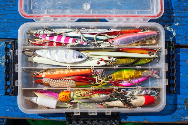 jig de cebo para la pesca de peces de mar en la caja de plástico en la mesa de madera azul