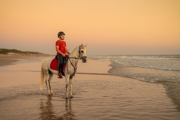 Jinete de 15 años monta su caballo blanco en la orilla del mar