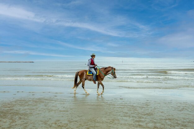 Jinete vestido de vaquero está jojjing en la playa de arena en Khao Takiab Hua Hin en Tailandia