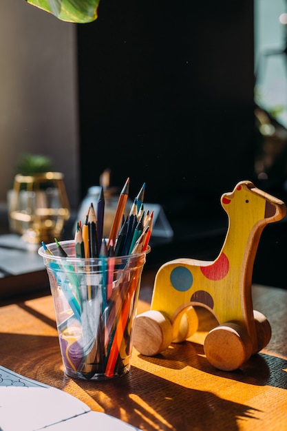 Foto jirafa de juguete de madera, lápices de colores y un libro para colorear sobre una mesa de madera