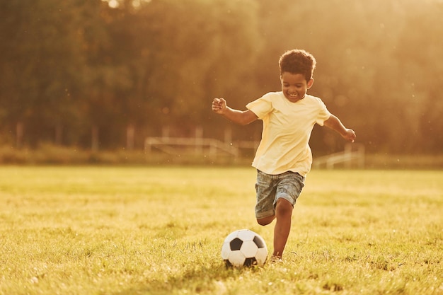 Joga futebol, criança afro-americana se diverte no campo no dia de verão