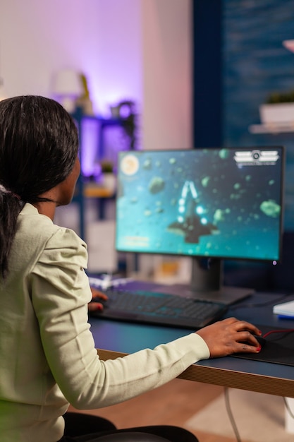Jogador africano tentando relaxar jogando campeonato online de atirador espacial. mulher competitiva do jogador cibernético realizando torneio de videogame usa joystick profissional.