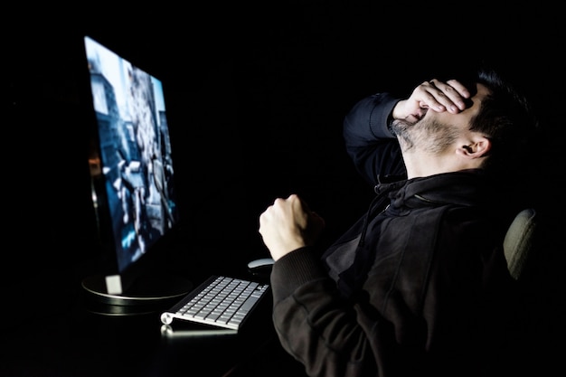 Jogador bonito do sexo masculino jogando videogame de computador à mesa no quarto escuro