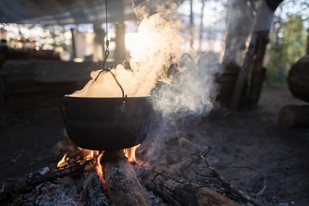 Jogador com vapor escapando paira sobre uma fogueira em que a comida é preparada ao pôr do sol