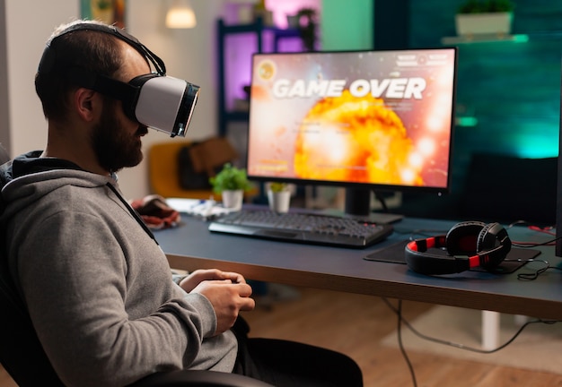 Jogador concentrado usando fone de ouvido de realidade virtual, perdendo jogos de tiro no espaço online. jogador derrotado usando o controle para competição online tarde da noite na sala de jogos