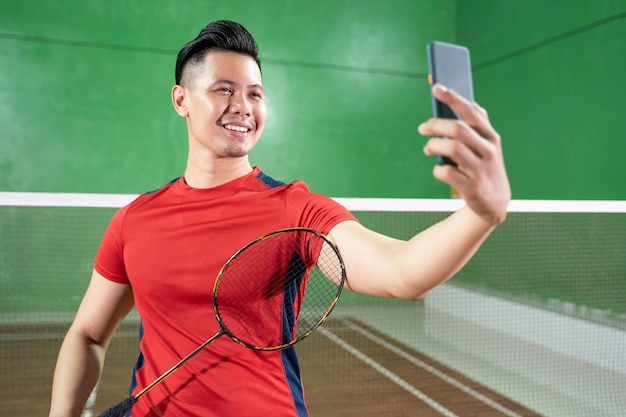 Jogador de badminton em vermelho segurando raquete enquanto tira selfie