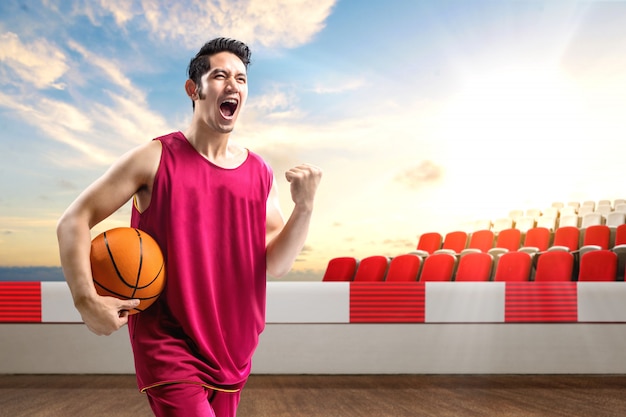 Jogador de basquete homem asiático, segurando a bola com uma expressão animada