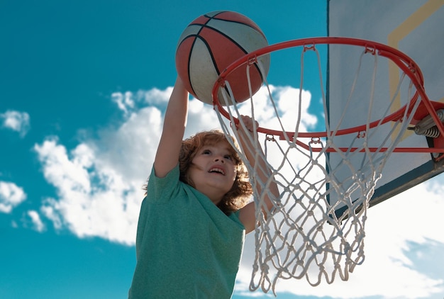 Jogador de basquete infantil fazendo enterrada no fundo do céu azul a criança praticando esportes