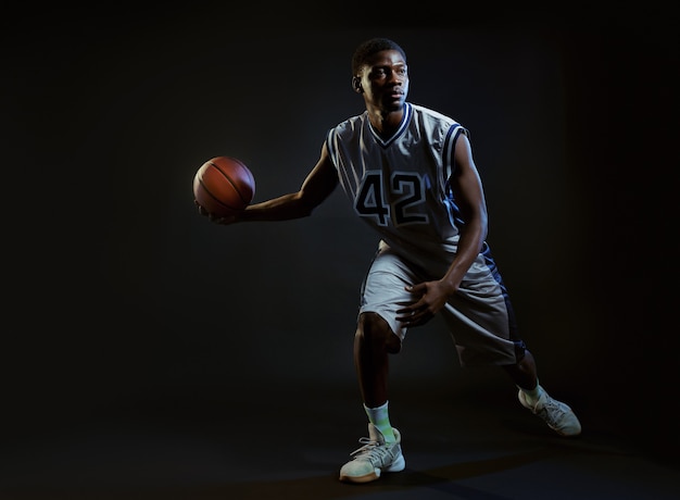 Jogador de basquete muscular com bola mostra sua habilidade. Baller profissional masculino em roupas esportivas, jogando esporte, esportista alto