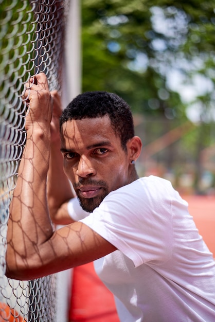 Jogador de basquete negro segurando a cerca de arame com as mãos