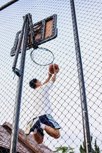 Jogador de basquete pulando alto para fazer uma enterrada na cesta atrás da cerca de malha