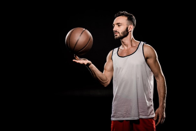 Foto jogador de basquetebol bonito girando a bola no dedo isolado em preto