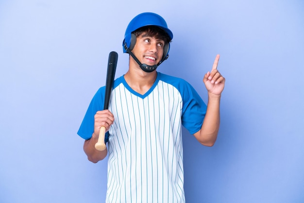 Jogador de beisebol caucasiano com capacete e taco isolado em fundo azul, apontando uma ótima ideia