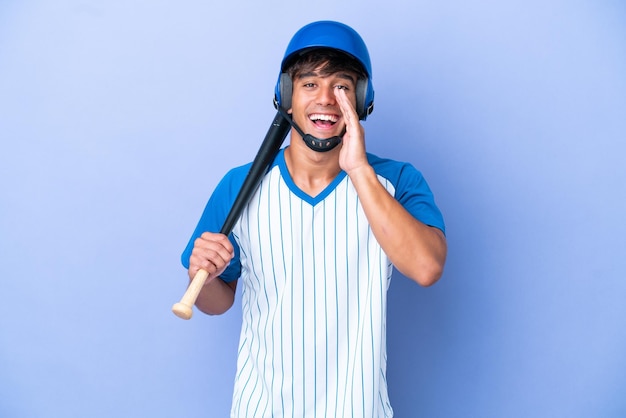 Jogador de beisebol caucasiano com capacete e taco isolado em fundo azul gritando com a boca aberta