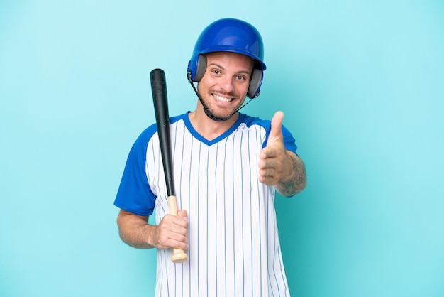 Jogador de beisebol com capacete e taco isolado em fundo azul apertando as mãos para fechar um bom negócio