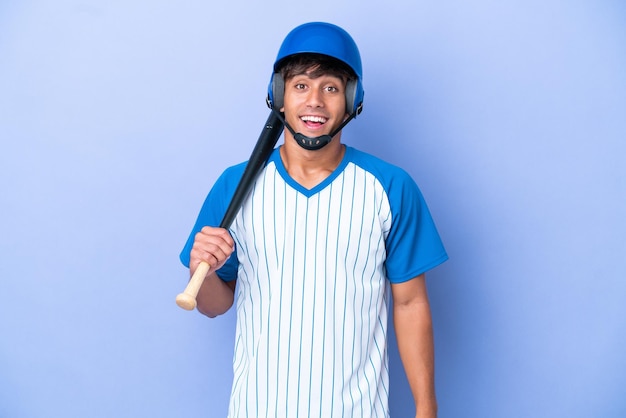 Jogador de beisebol homem caucasiano com capacete e taco isolado em fundo azul com expressão facial de surpresa