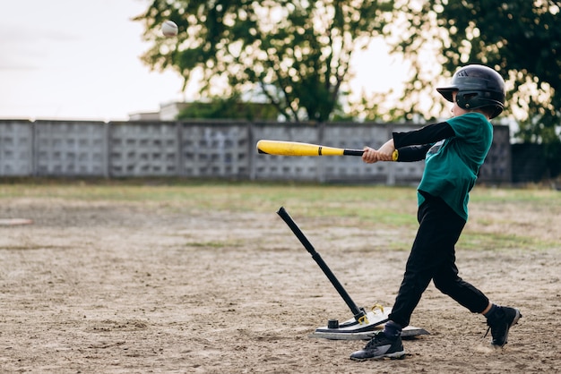 Jogador de beisebol pequeno bonito bate a bola com um taco de beisebol