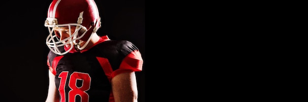 Jogador de futebol americano com capacete em pé contra um fundo preto