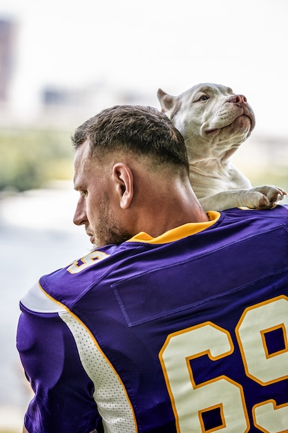 Jogador de futebol americano com um cachorro posando na câmera em um parque. copyspace, bandeira de esportes. futebol americano, esporte para a proteção de animais.