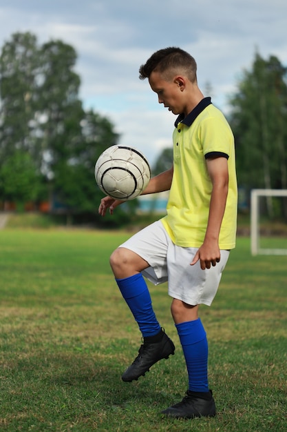 Foto jogador de futebol bonito com uma camiseta amarela no campo de futebol fazendo malabarismos com a bola