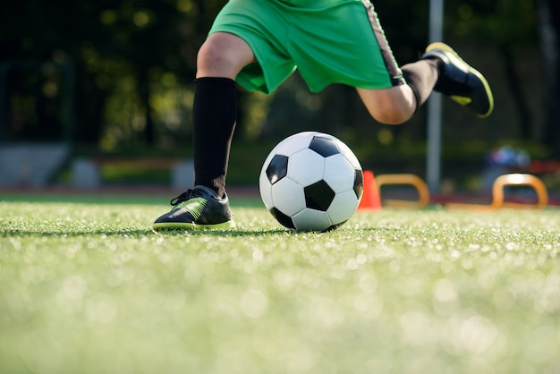 Jogador de futebol chutando a bola no campo. Jogadores de futebol na sessão de treinamento. Feche os pés do jogador de futebol chutando a bola na grama.