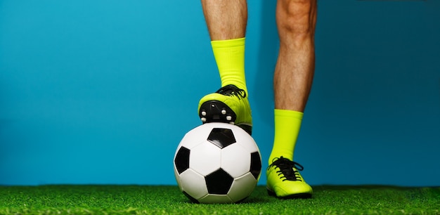Jogador de futebol com bola na grama verde e fundo azul