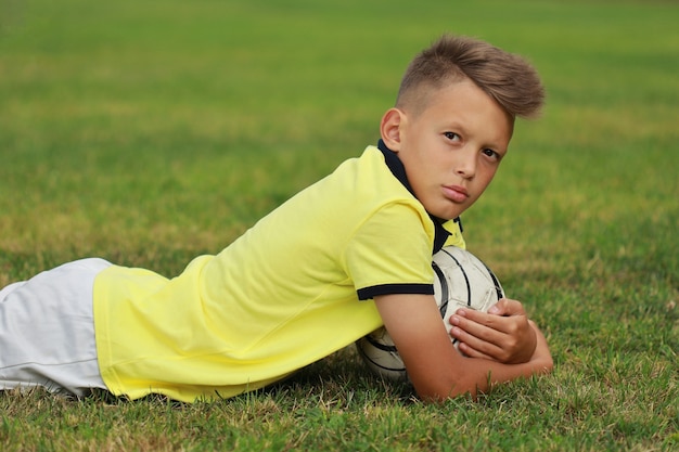 Foto jogador de futebol de menino bonito deitado no campo de futebol com a bola