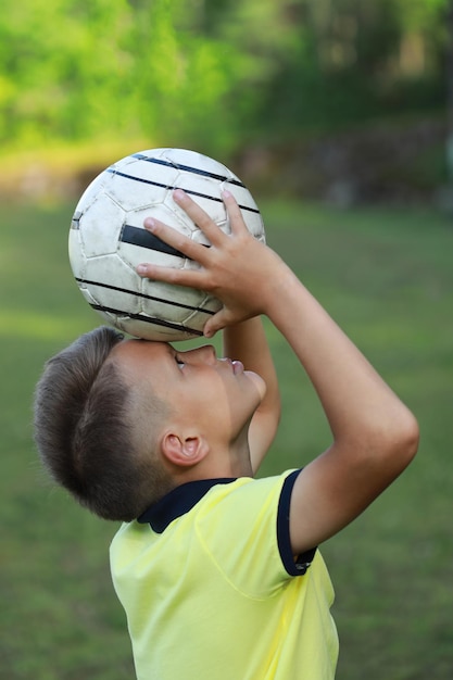 jogador de futebol de menino bonito em uma camiseta amarela em um campo de futebol com uma bola