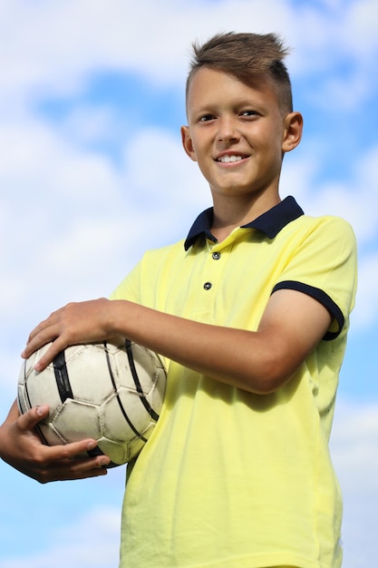 Jogador de futebol de menino bonito em uma camiseta amarela tem a bola nas mãos. contra o céu