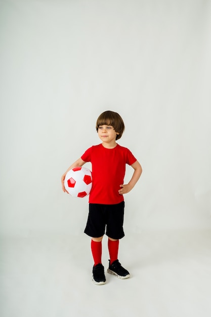 Jogador de futebol do menino está com uma bola de futebol em uma superfície branca com espaço para texto. esportes para crianças